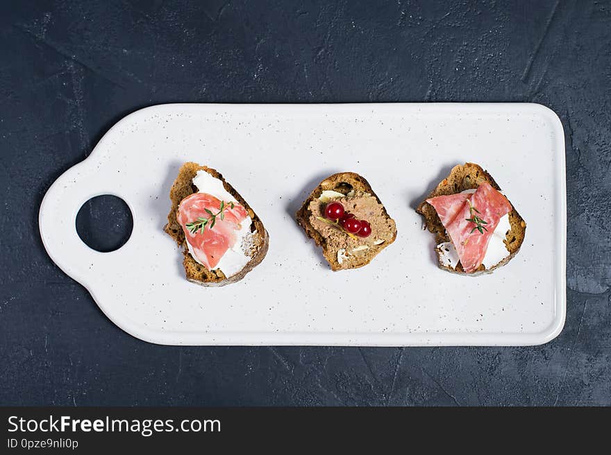 Toast with Parma, salami and goose pate on a white chopping Board.