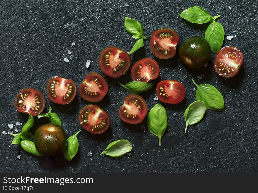 Food background, black and red cherry tomatoes and green basil on a wet  stone background, top view