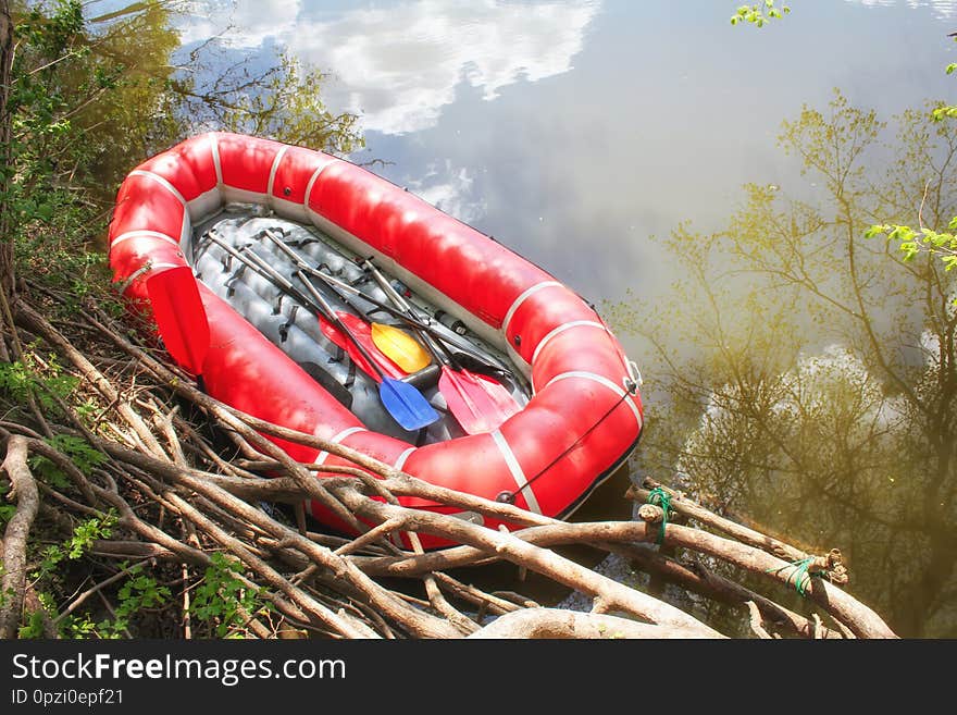 Red inflatable boat with oars raft for rafting along a  river against the sky reflected in the water. View from above