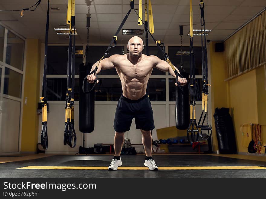 Man bodybuilder perform exercise with TRX in GYM