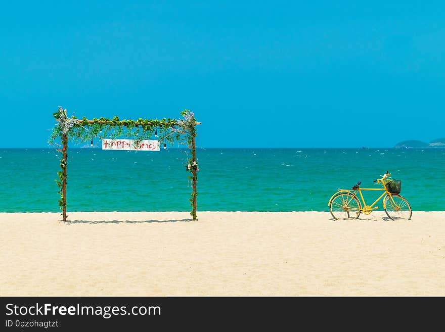 Wooden gate with flowers and old yellow bicycle on beach