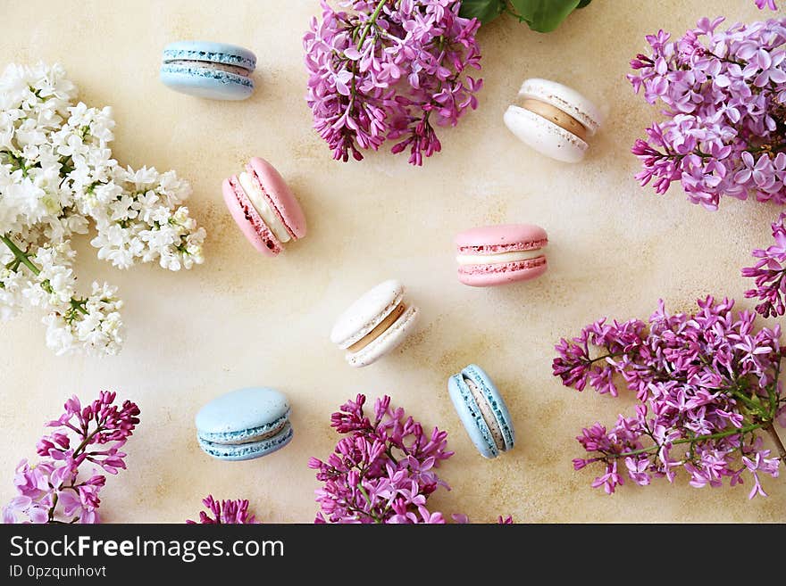 Minimalistic composition with bunch of french macaron sweets of different color and taste, lilac flowerings scattered over yellow concrete texture background. Top view, close up, flat lay, copy space. Minimalistic composition with bunch of french macaron sweets of different color and taste, lilac flowerings scattered over yellow concrete texture background. Top view, close up, flat lay, copy space