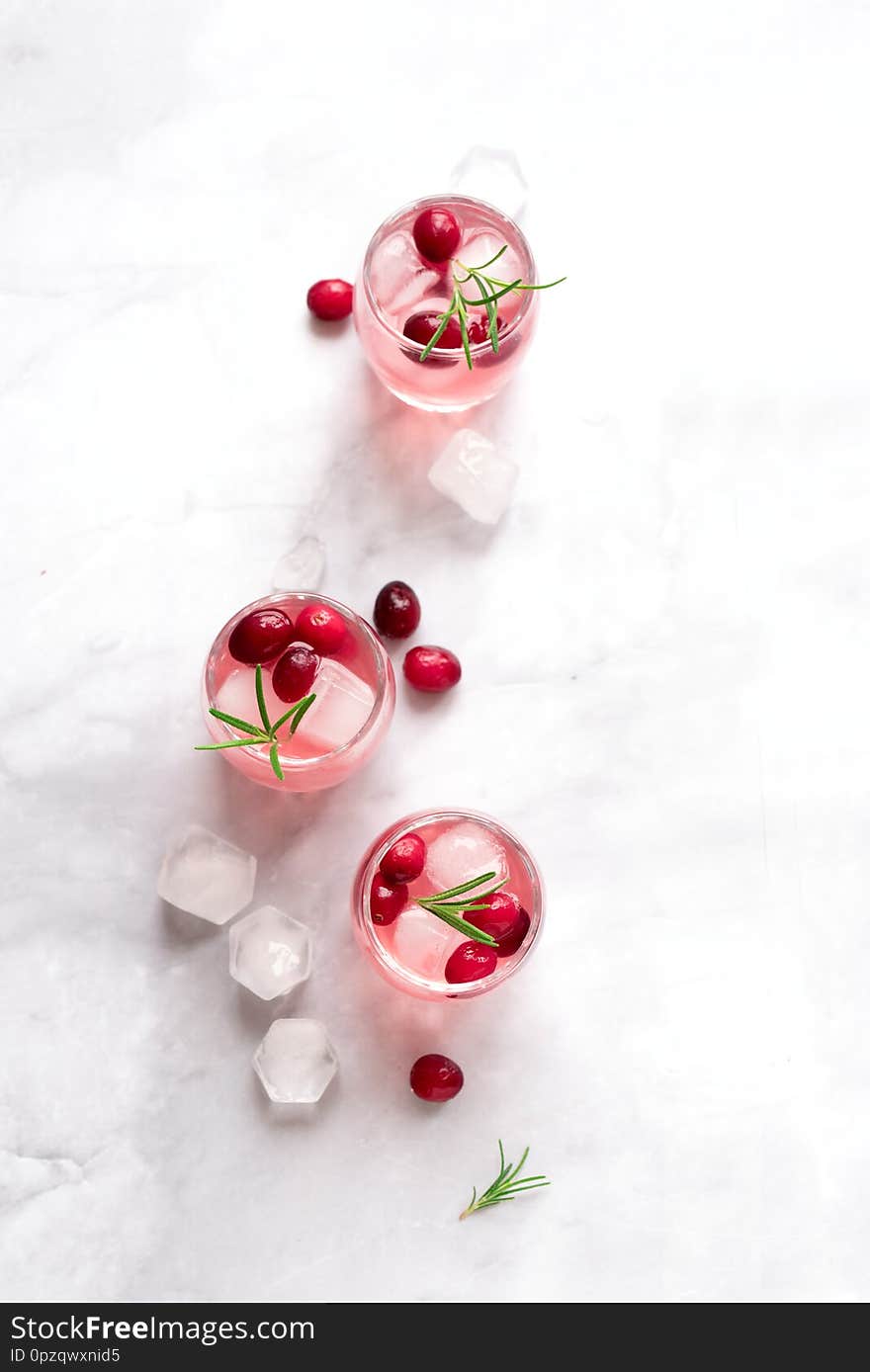 Cranberry Vodka Cocktail with ice cubes and rosemary on white marble background, copy space. Homemade alcohol cocktail with cranberries