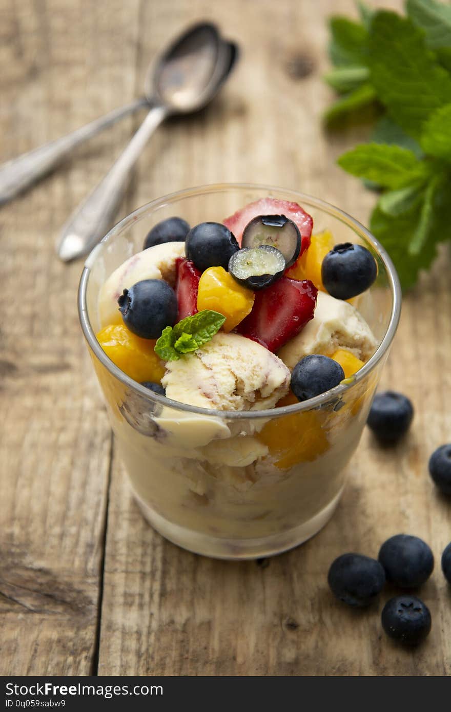 Vanilla ice cream with fruits - blueberries, strawberries, mango and mint, summer refreshing dessert. Wooden background. Glass with vanilla ice cream