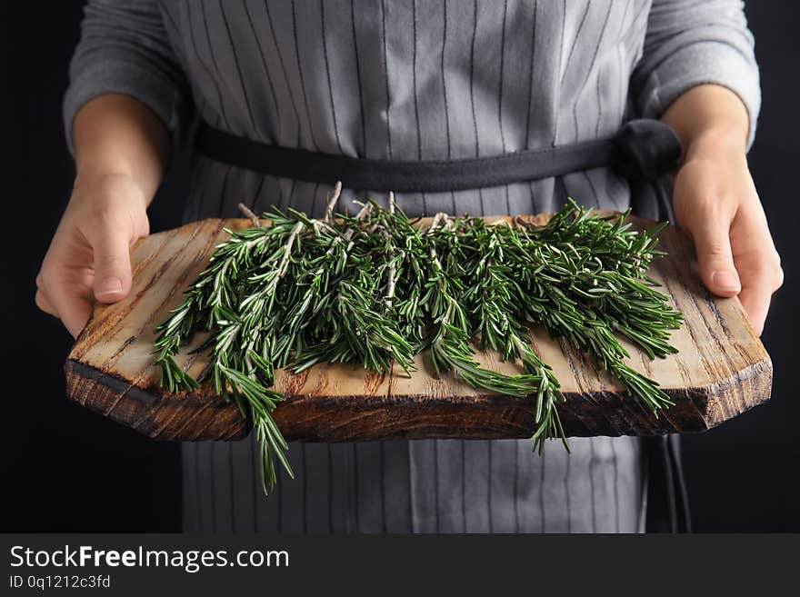 Woman holding wooden board with fresh rosemary twigs on black background