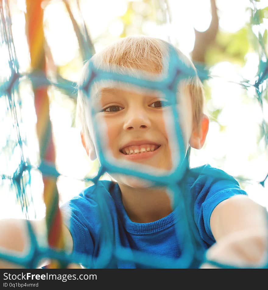 Happy child climbing on a playground ropes. Cheerful little boy playing on modern playground. Smiling kid having fun at adventure