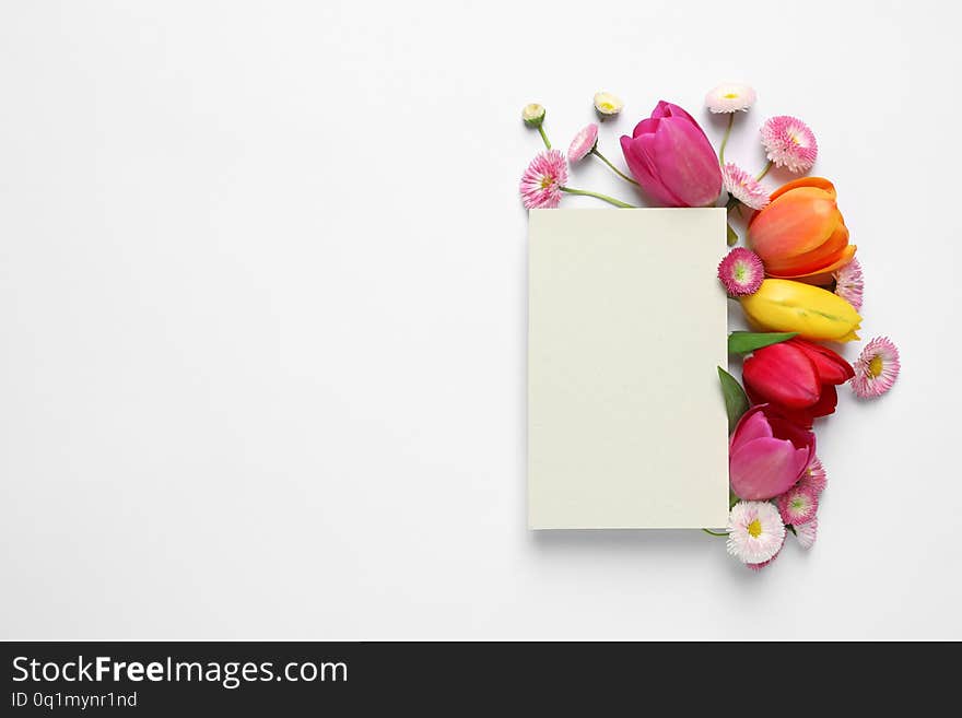 Beautiful composition with spring flowers and blank card on white background, top view. Space for text