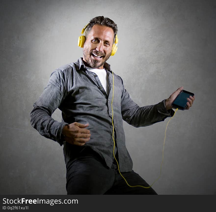 Natural portrait of 40s happy and excited attractive man listening online music  with headphones and mobile phone singing song and dancing carefree isolated on grunge studio background