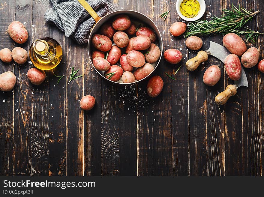 Raw organic potatoes, ingredients for healthy cooking on old rustic wooden background. Spices, oil and rosemary. Top view. Country food concept. Raw organic potatoes, ingredients for healthy cooking on old rustic wooden background. Spices, oil and rosemary. Top view. Country food concept