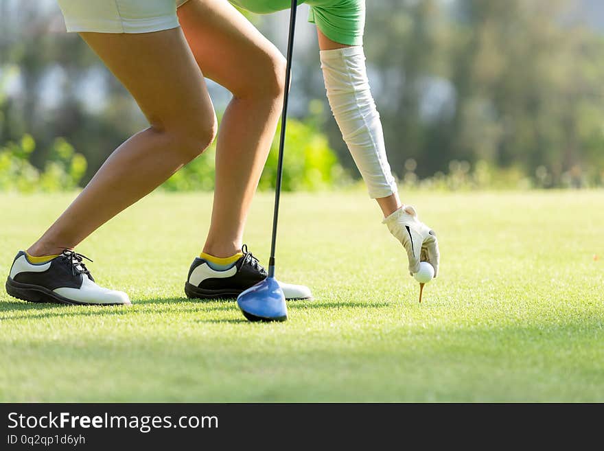 Hand asian sporty woman putting golf ball on tee with club in golf course on evening on time for healthy sport. Lifestyle and Sport Concept