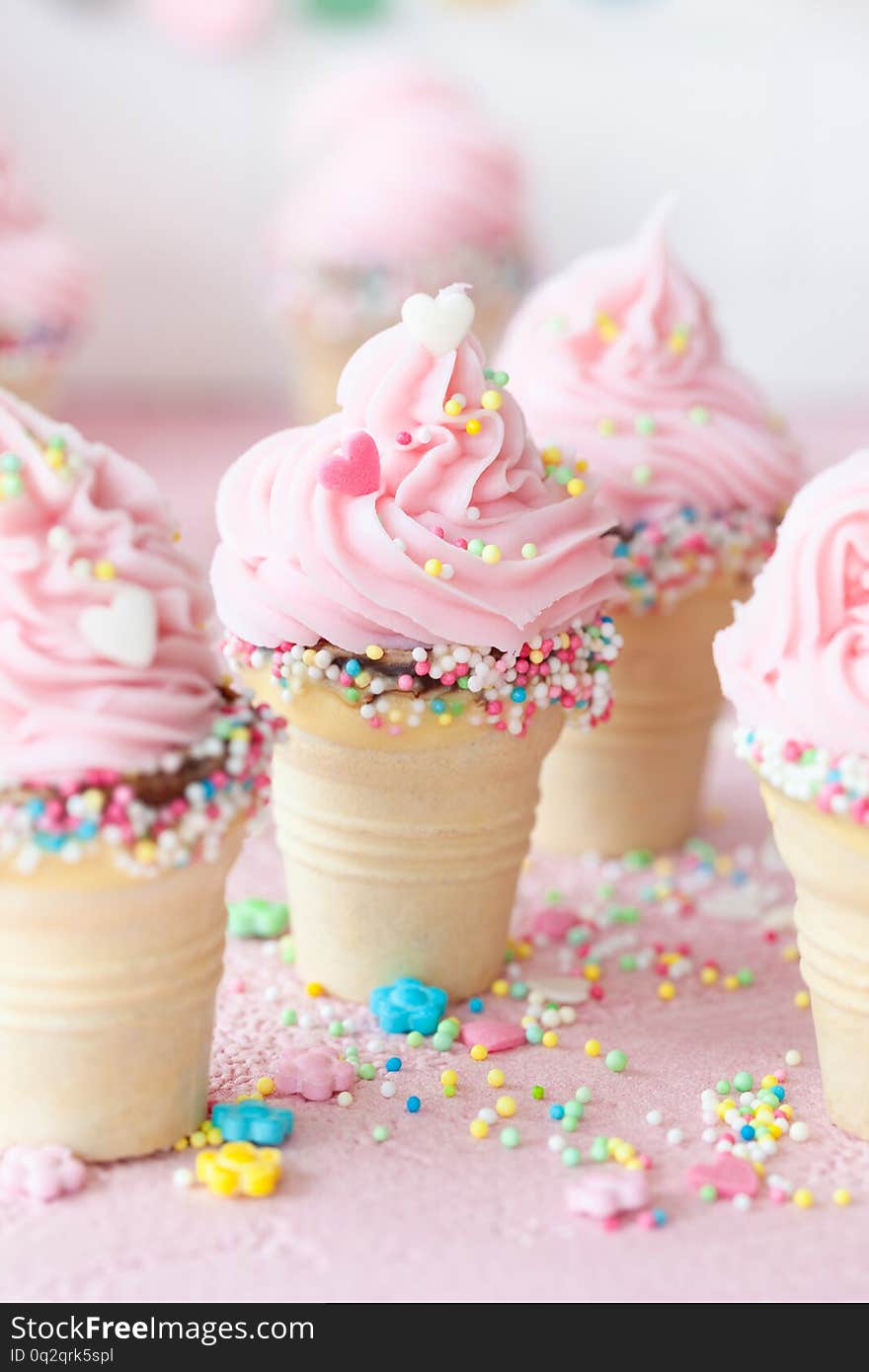 Pink soft serve ice cream with colorful sprinkles in little waffle cups. Pink soft serve ice cream with colorful sprinkles in little waffle cups