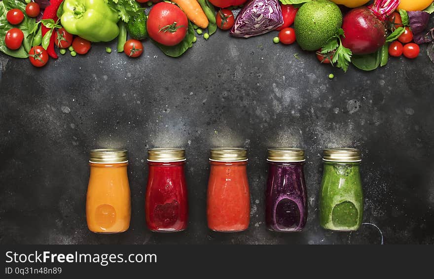 Food and drink background. Colorful vegan vegetable juices and smoothies set in bottles on gray kitchen table, copy space, selective focus