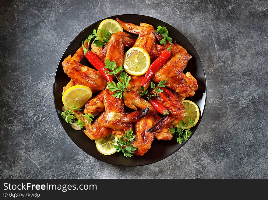 Delicious grilled chicken wings with lemon juice and chili pepper on gray concrete background. Top view. Copy cpace.   food