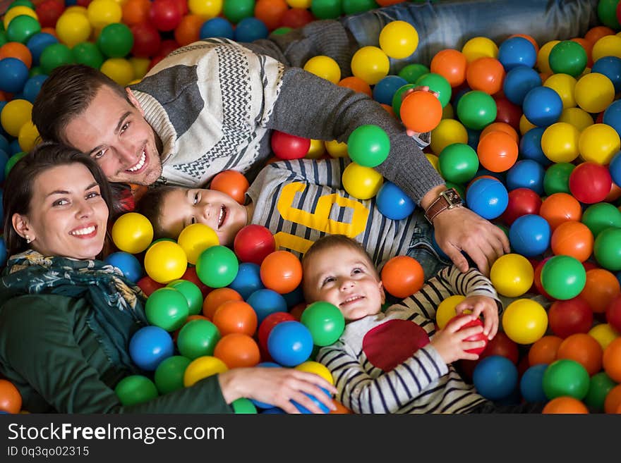 Happy family enjoying free time young parents and kids playing in the pool with colorful balls at childrens playroom