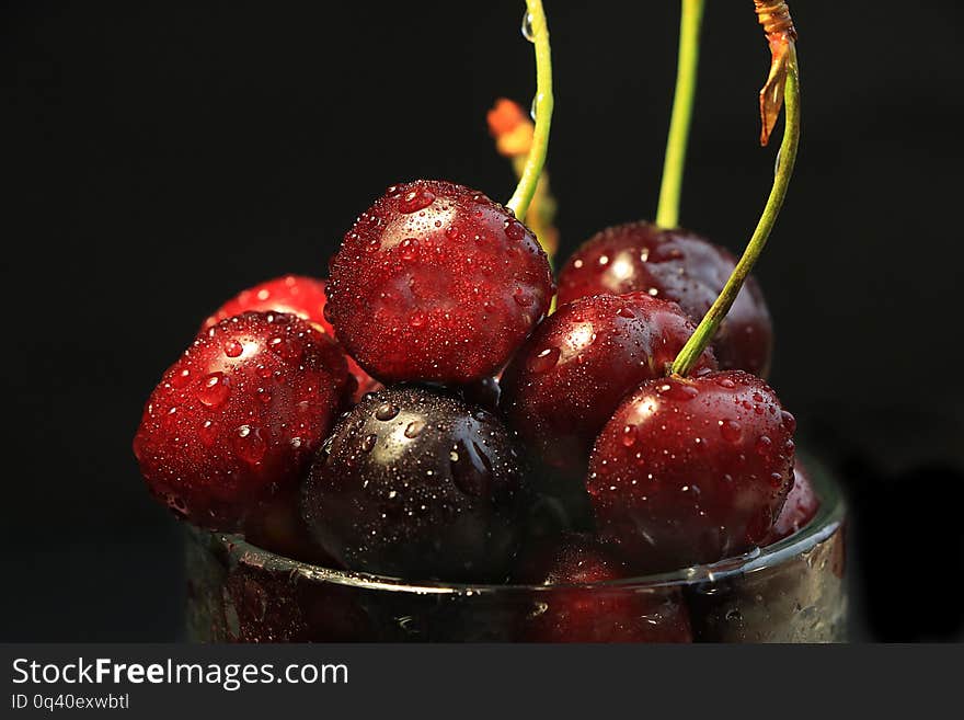 Juicy red cherry with drops on a black background close-up, selective focus. Delicious beautiful berries in a glass after washing make you want to eat them