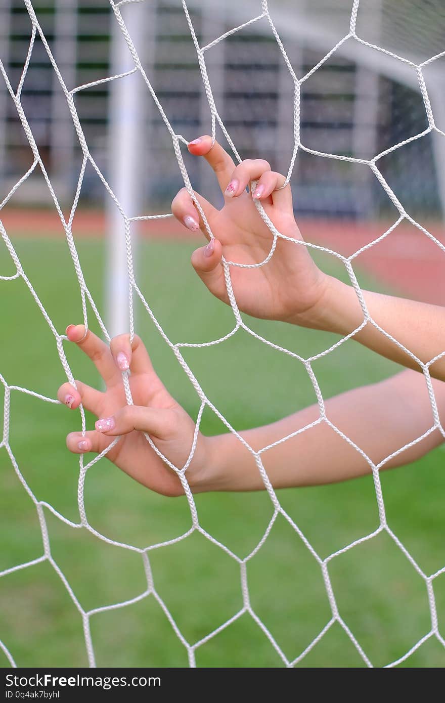 Hand hold on net of soccer goal on sport field.