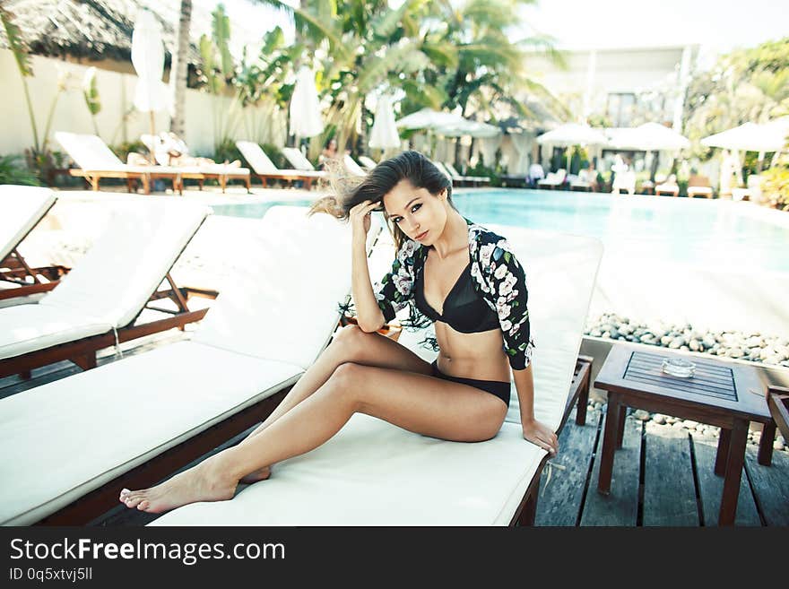 Young pretty woman at swimming pool relaxing in chair, fashion look in lingerie at hotel, lifestyle people concept