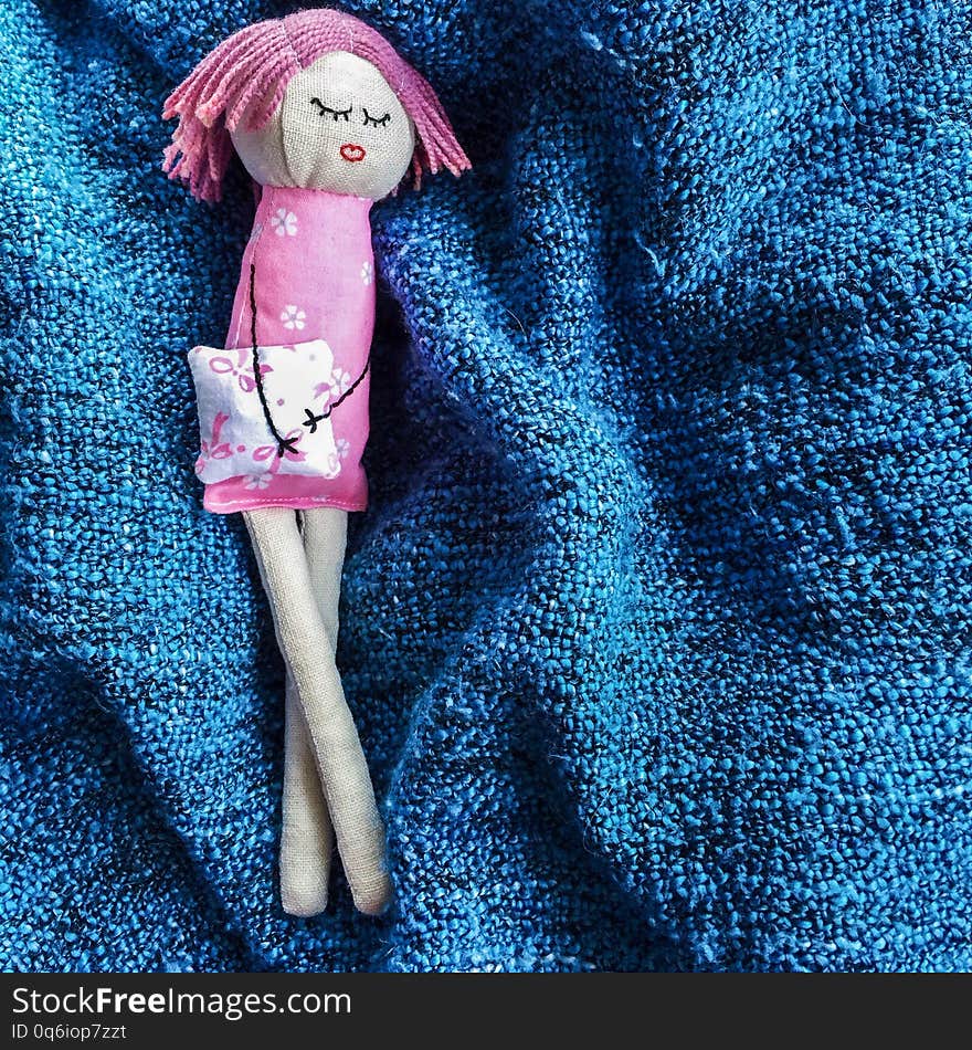 Little sleeping handmade doll made of linen and cotton lying with crossed legs on a blue plaid