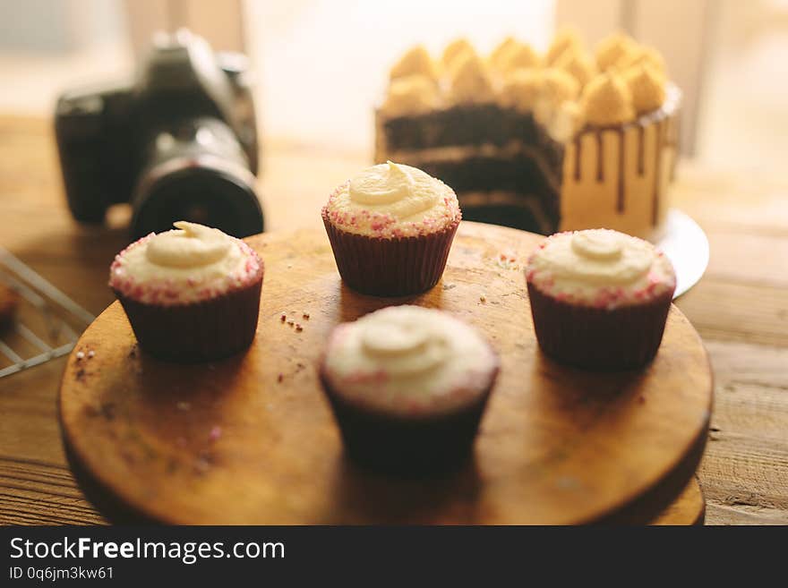 Cupcakes on wooden board with cake and camera on table at the back. Cupcakes on wooden board with cake and camera on table at the back