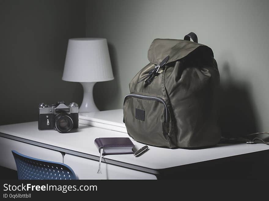 Backpack, camera, laptop, notebook and pen on the desk in the room