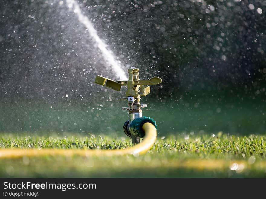 Watering lawn in garden. Splashing drops from hose and gardening sprayer. Watering lawn in garden. Splashing drops from hose and gardening sprayer