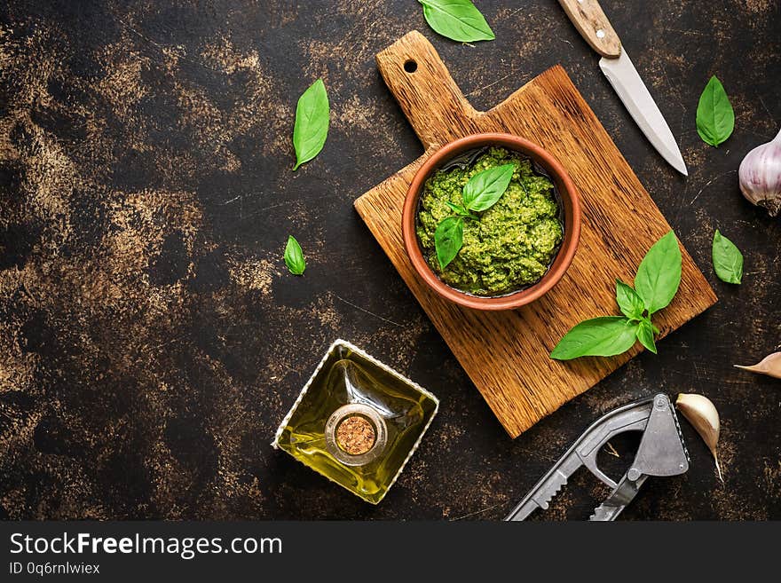 Pesto sauce, basil leaves, garlic and olive oil on a dark rustic background. Overhead view,copy space