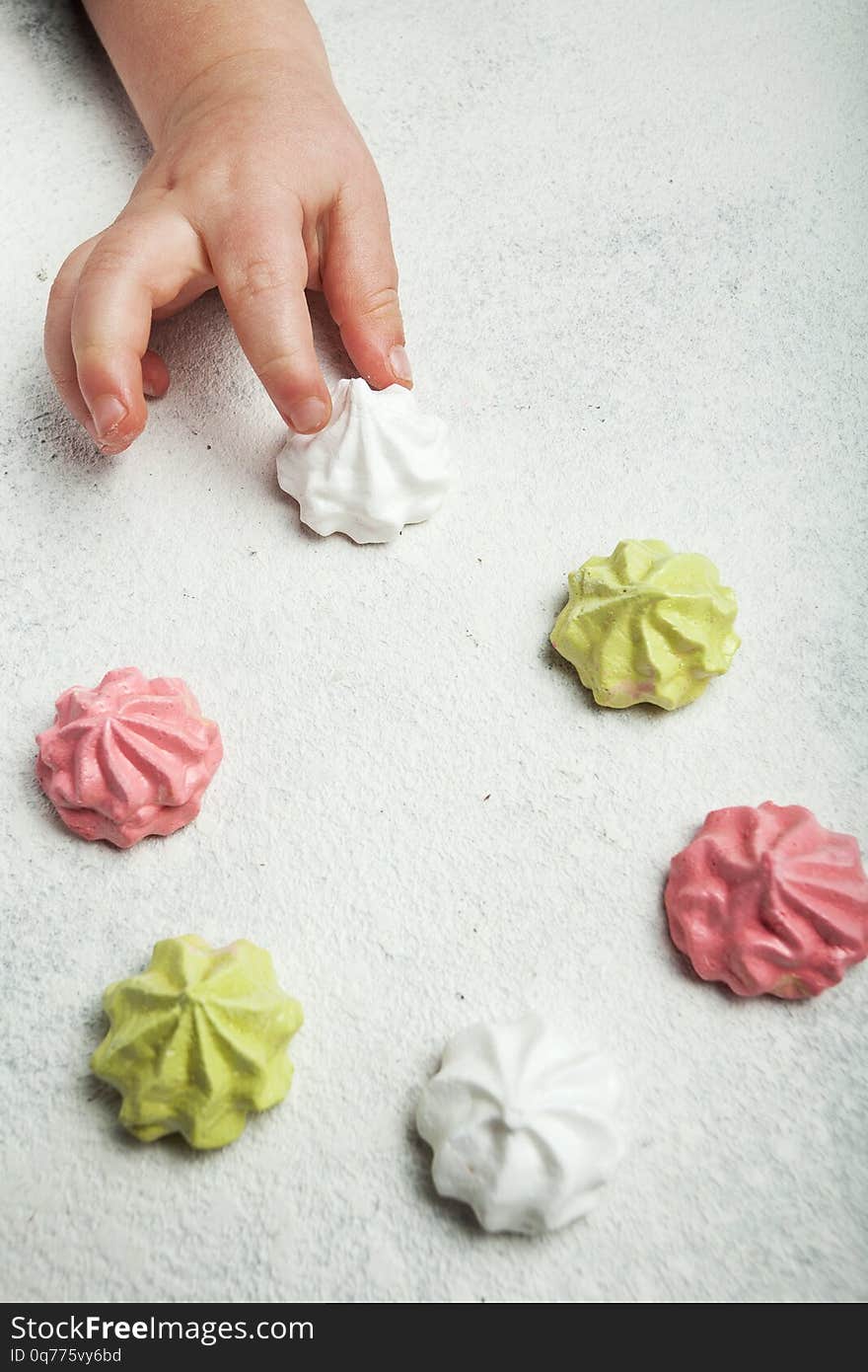 Little baby hand takes a French sweet meringue dessert on a white retro background, vertically.