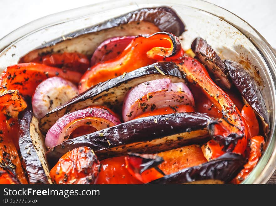 Baked vegetables tomatoes, eggplants, blue onions, zucchini, zucchini in glass form on a bright white background. The concept of proper healthy and healthy food