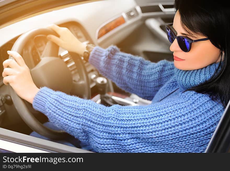 A beautiful pretty brunette woman in a blue sweater and sunglasses is driving a car. Toned