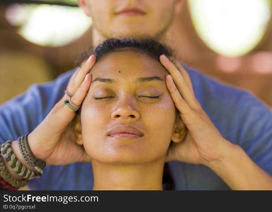 Natural lifestyle portrait of young beautiful and relaxed Asian Balinese woman receiving a healing facial and head Thai massage by