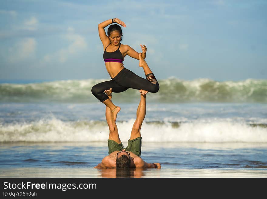 Outdoors lifestyle portrait young attractive and concentrated couple of yoga acrobats practicing acroyoga balance and meditation exercise on beautiful beach in mind and body teamwork control