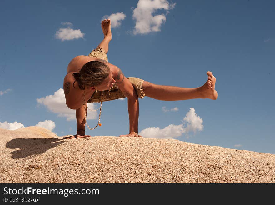 Male yogi hand balancing in Flying Splits or in Sanskrit Eka Pada Koundinyasana on a boulder field on a sunny cloud filled day. This pose is dedicated to the sage Koundinya II. Photographed in  Joshua Tree, CA a wilderness desert environment. Male yogi hand balancing in Flying Splits or in Sanskrit Eka Pada Koundinyasana on a boulder field on a sunny cloud filled day. This pose is dedicated to the sage Koundinya II. Photographed in  Joshua Tree, CA a wilderness desert environment.