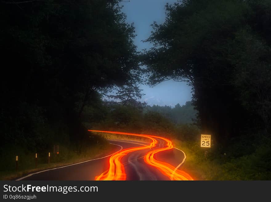 Orange, red and yellow car light trails along a road curve in the mountains at night with speed limit sign. Transportation, driving and safety concept