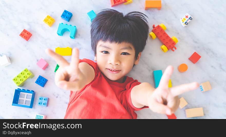 Boy surrounded by colorful toy blocks top view V shape hand for victory