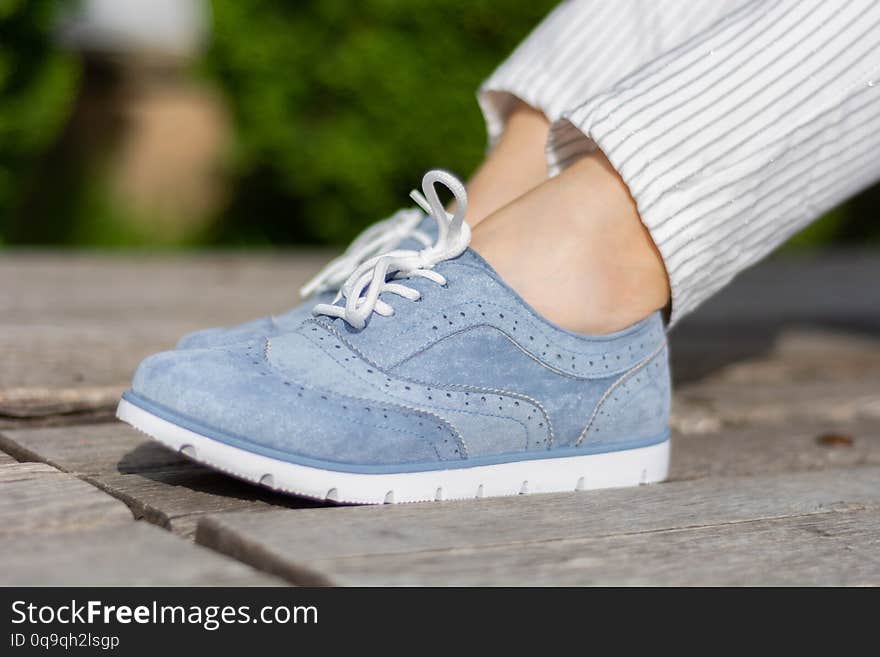 Girl legs with blue sneakers on a wooden bench in the park on a spring day