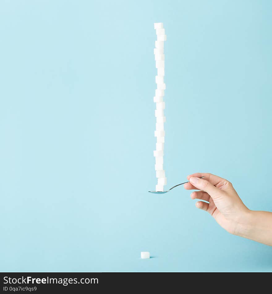 Female hand holding a spoon with column made of sugar cubes. Sweet life concept, minimal style. Sugar offering. Female hand holding a spoon with column made of sugar cubes. Sweet life concept, minimal style. Sugar offering
