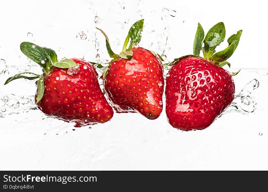 Ripe red strawberries are thrown and dropped into sparkling water, many bubbles.