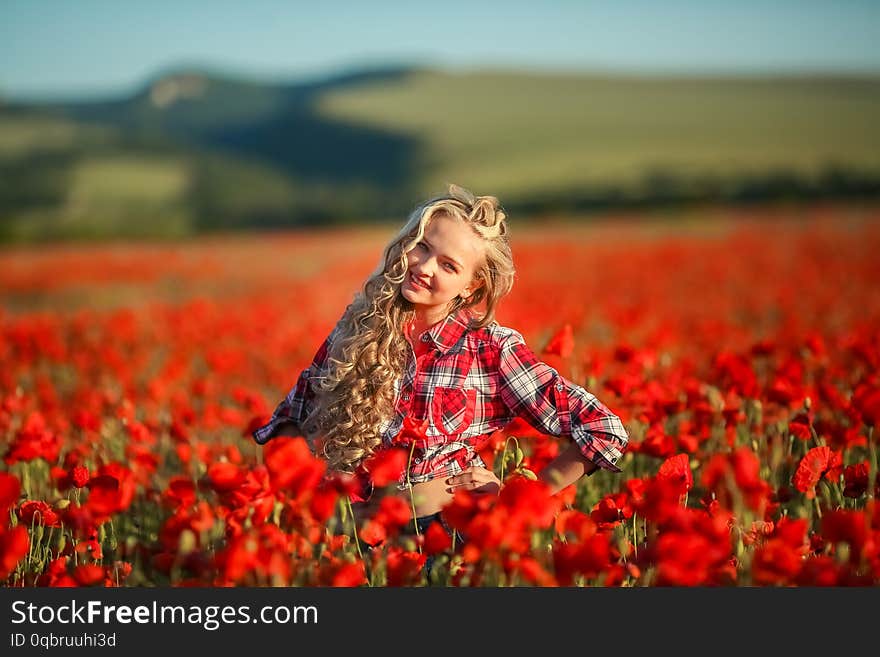 Young blonde in a red shirt in the poppy flower field.