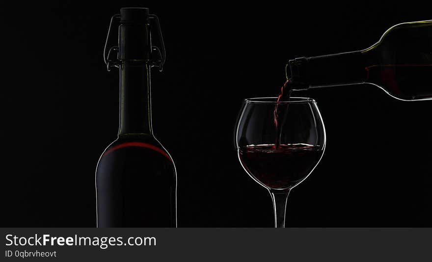 Wine. Red wine pouring in wine glass over black background. Rose wine pour from the bottle. Silhouette. Close up shot. Wine. Red wine pouring in wine glass over black background. Rose wine pour from the bottle. Silhouette. Close up shot