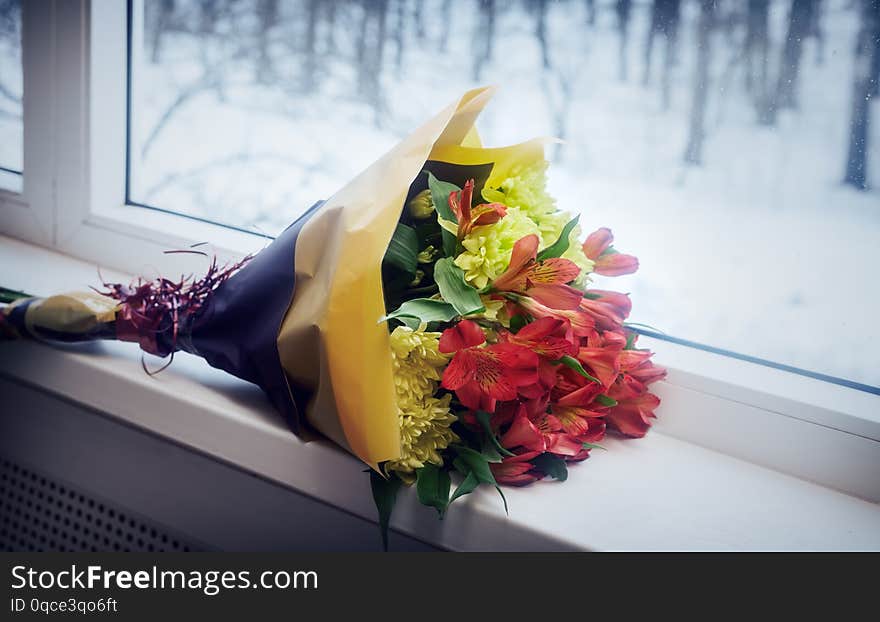 On the windowsill lies a beautifully packaged bouquet of fresh chrysanthemum and Amaryllis flowers. Outside the window winter landscape. On the windowsill lies a beautifully packaged bouquet of fresh chrysanthemum and Amaryllis flowers. Outside the window winter landscape