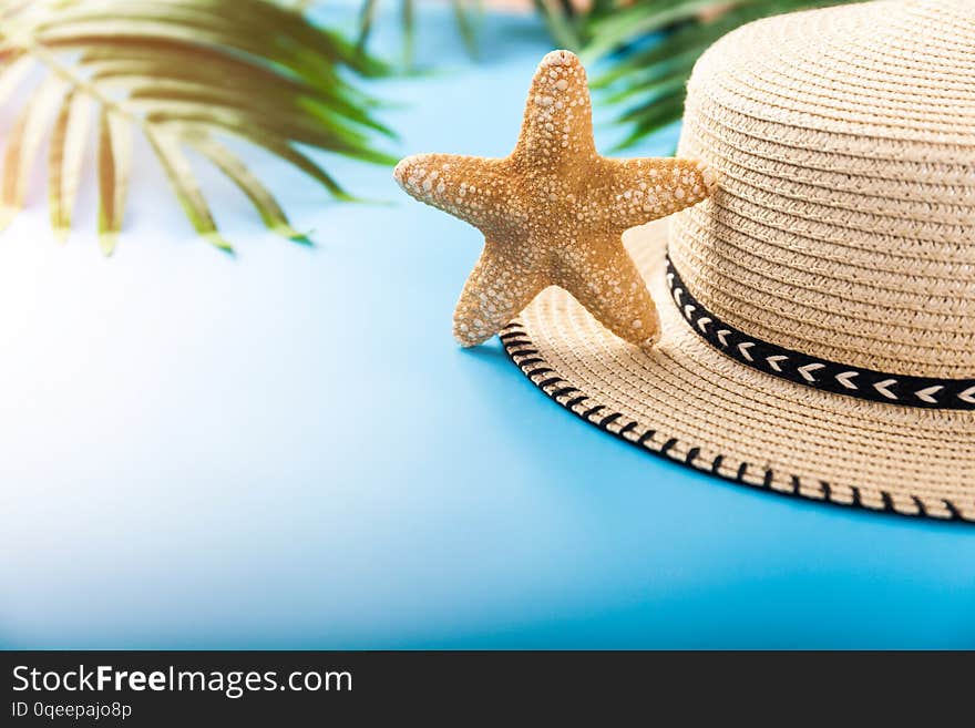 Summer holiday background. Beach accessories: starfish, tropical palm leaves, straw hat on blue background. Vacation and travel items. Summer concept. Front view. Summer holiday background. Beach accessories: starfish, tropical palm leaves, straw hat on blue background. Vacation and travel items. Summer concept. Front view