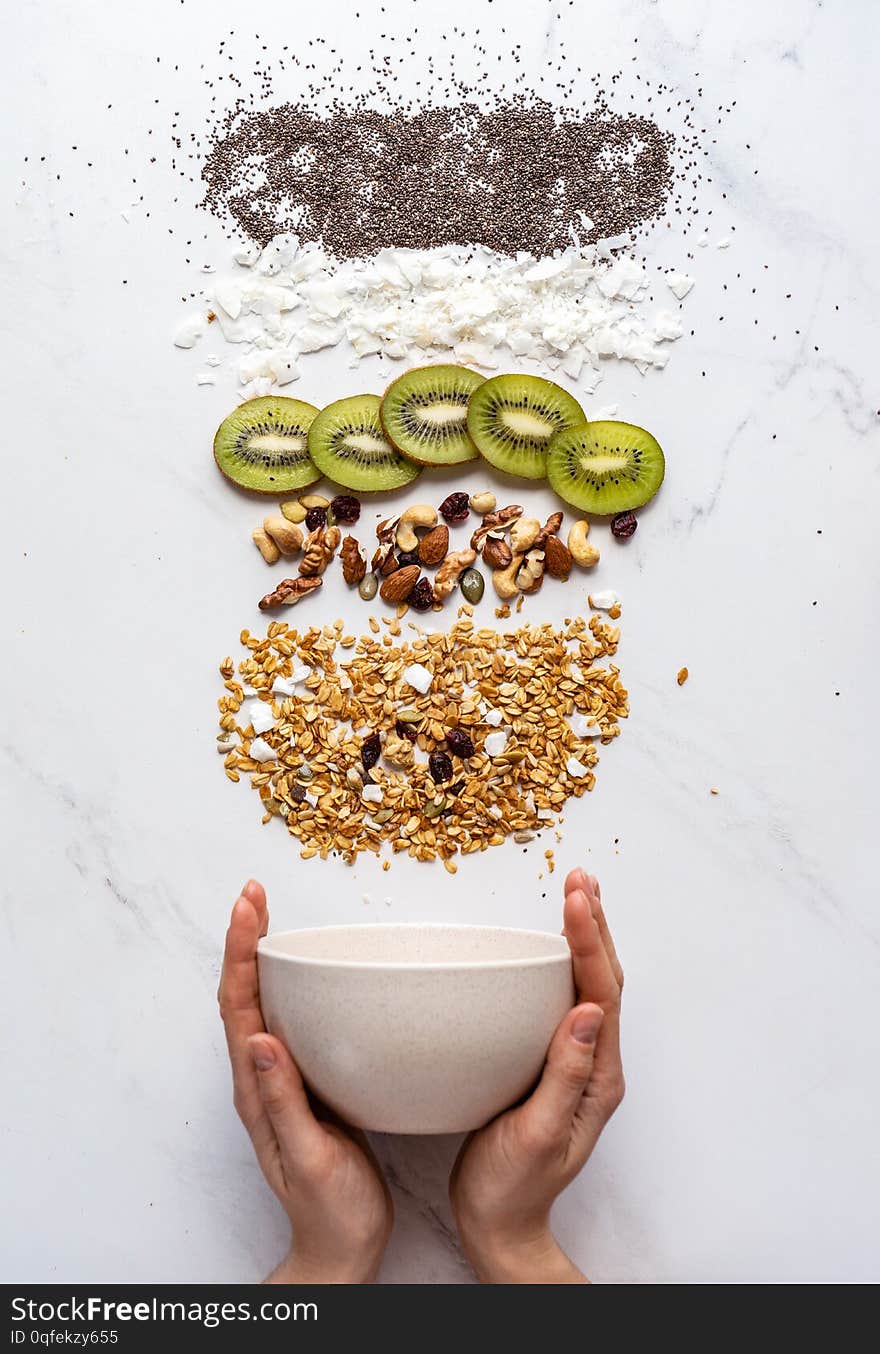 Healthy breakfast concept, female hand holding bowl with granola nuts kiwi chia seeds on white background, morning organic food with diet on table, detox meal for health nutrition vertical top view