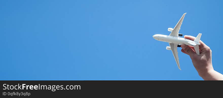 Hand holding airplane model in front of blue sky background. Travel