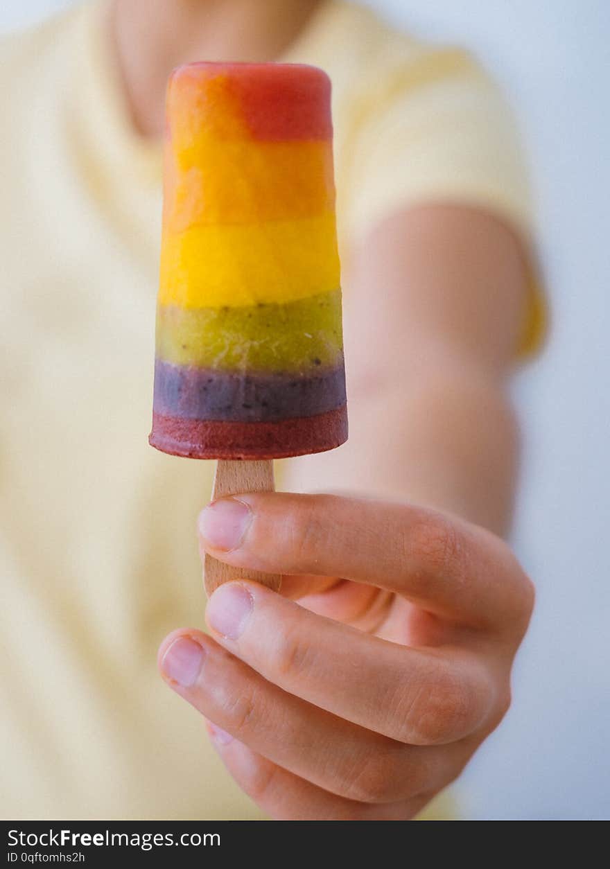 Girl with a yellow t-shirt holding a rainbow popsicle in her hands. Girl with a yellow t-shirt holding a rainbow popsicle in her hands