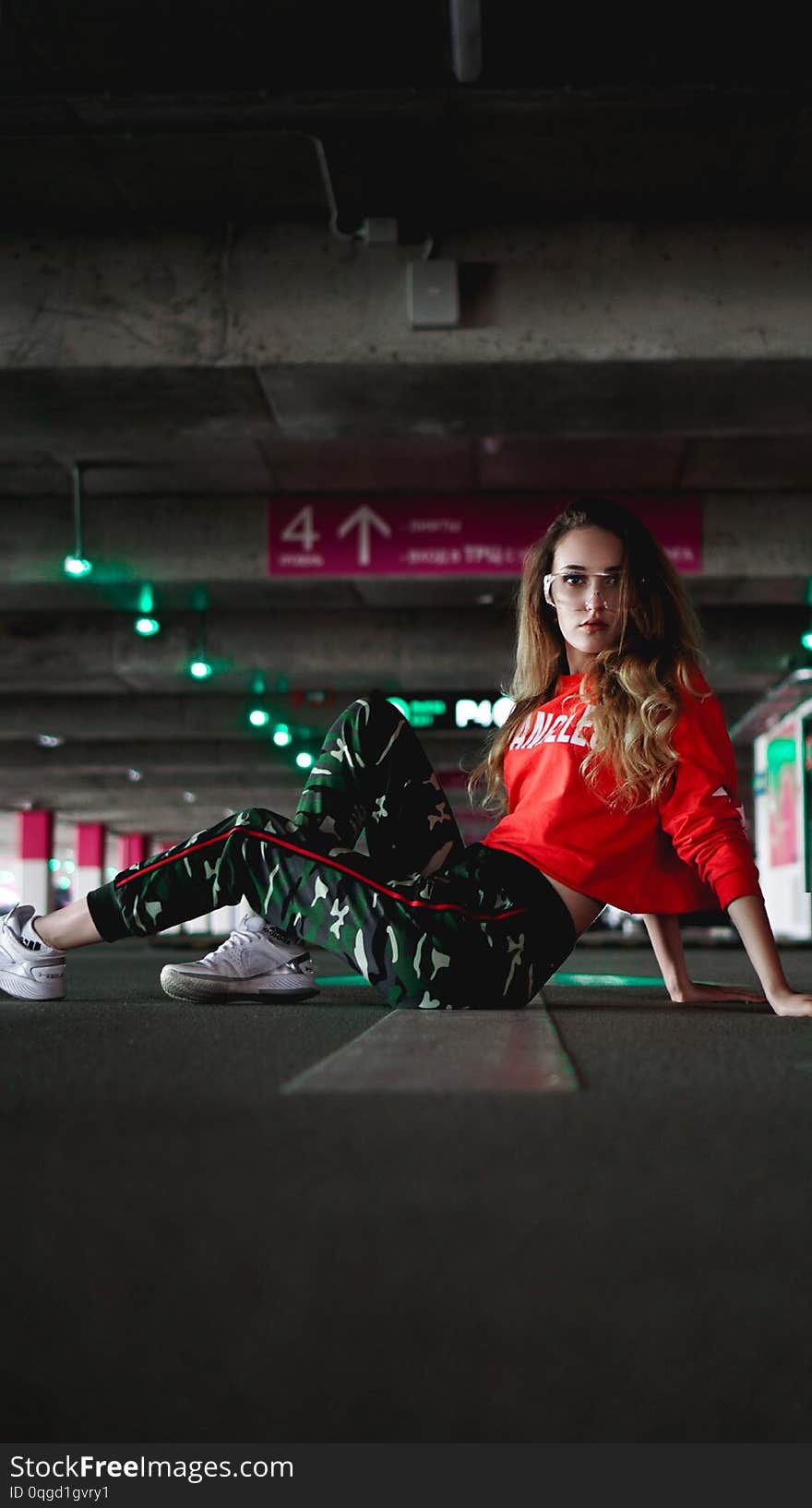 Pretty young woman sitting on car parking. Wearing stylish urban outfit