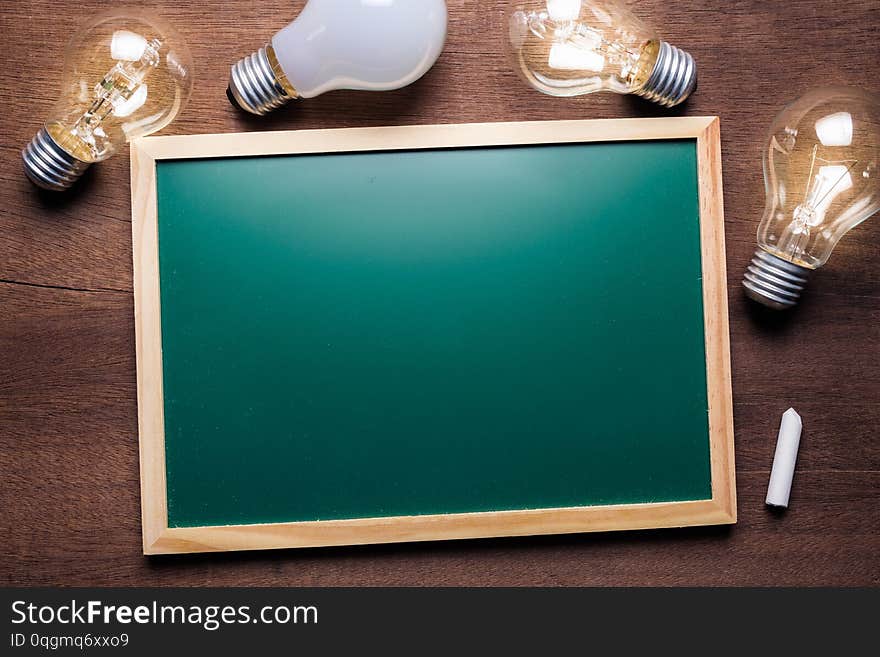 Small blackboard frame with glowing light bulbs on wood background. Small blackboard frame with glowing light bulbs on wood background