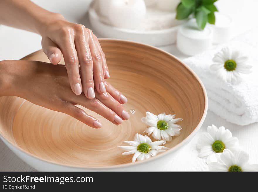 Woman soaking her hands in bowl of water and flowers on table, closeup with space for text. Spa treatment. Woman soaking her hands in bowl of water and flowers on table, closeup with space for text. Spa treatment