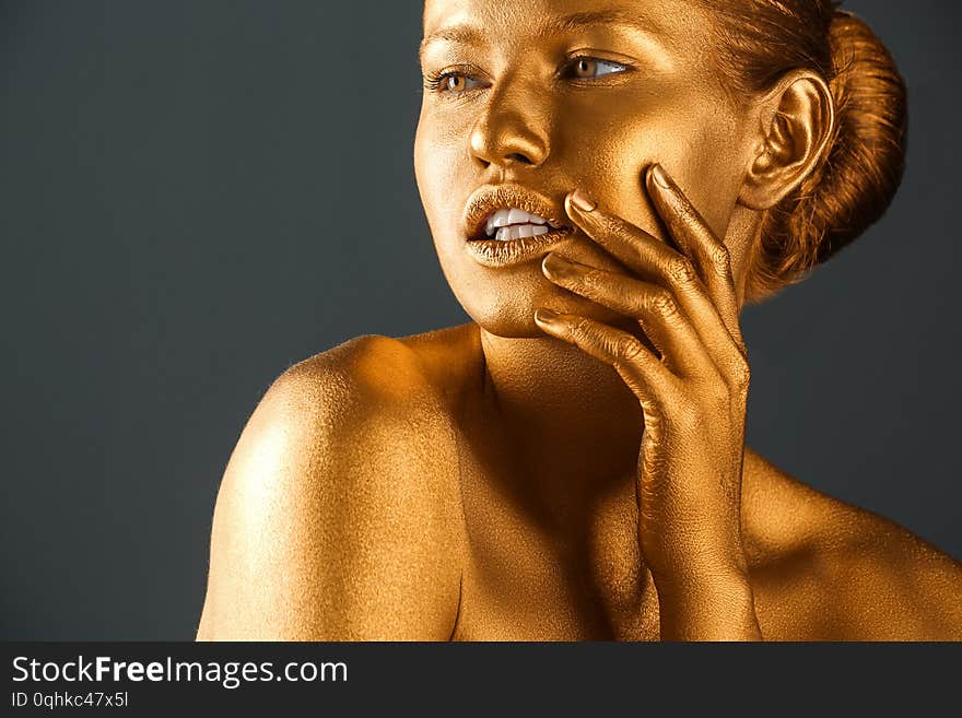 Portrait of beautiful lady with gold paint on skin against grey background, closeup