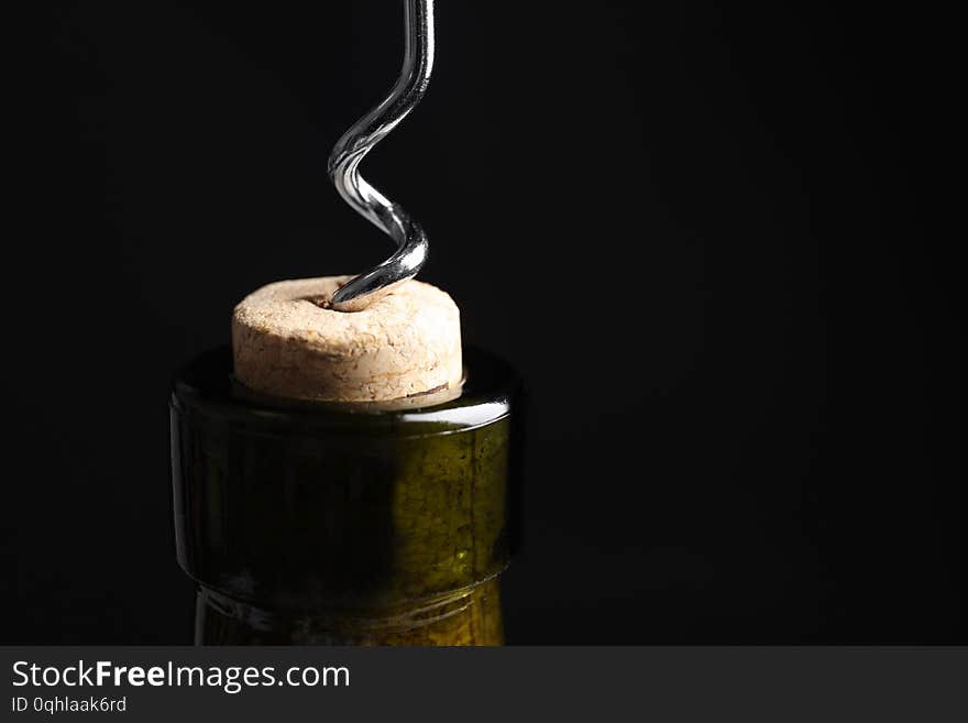 Opening wine bottle with corkscrew on black background, closeup