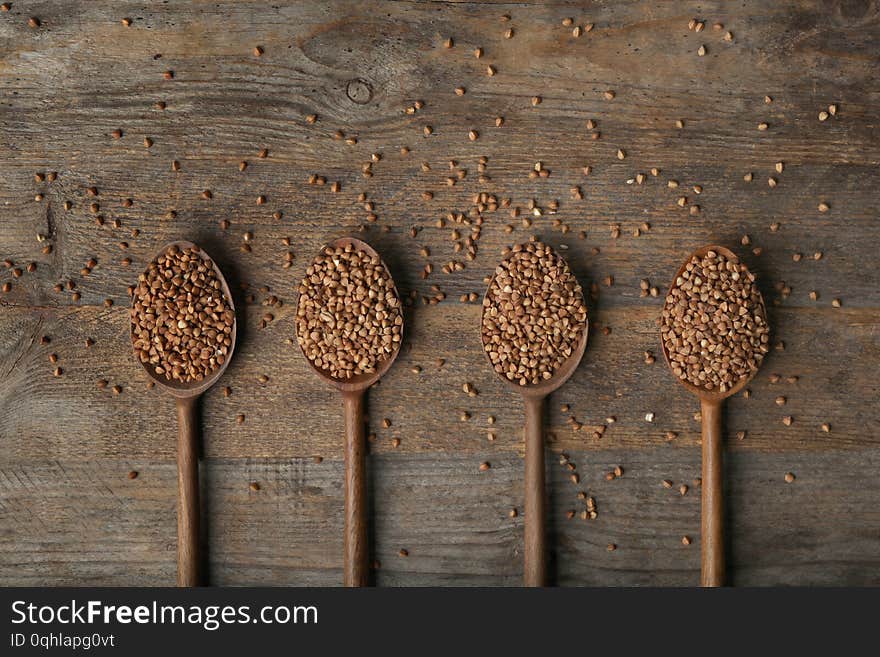 Spoons with uncooked buckwheat on wooden table, flat lay. Space for text